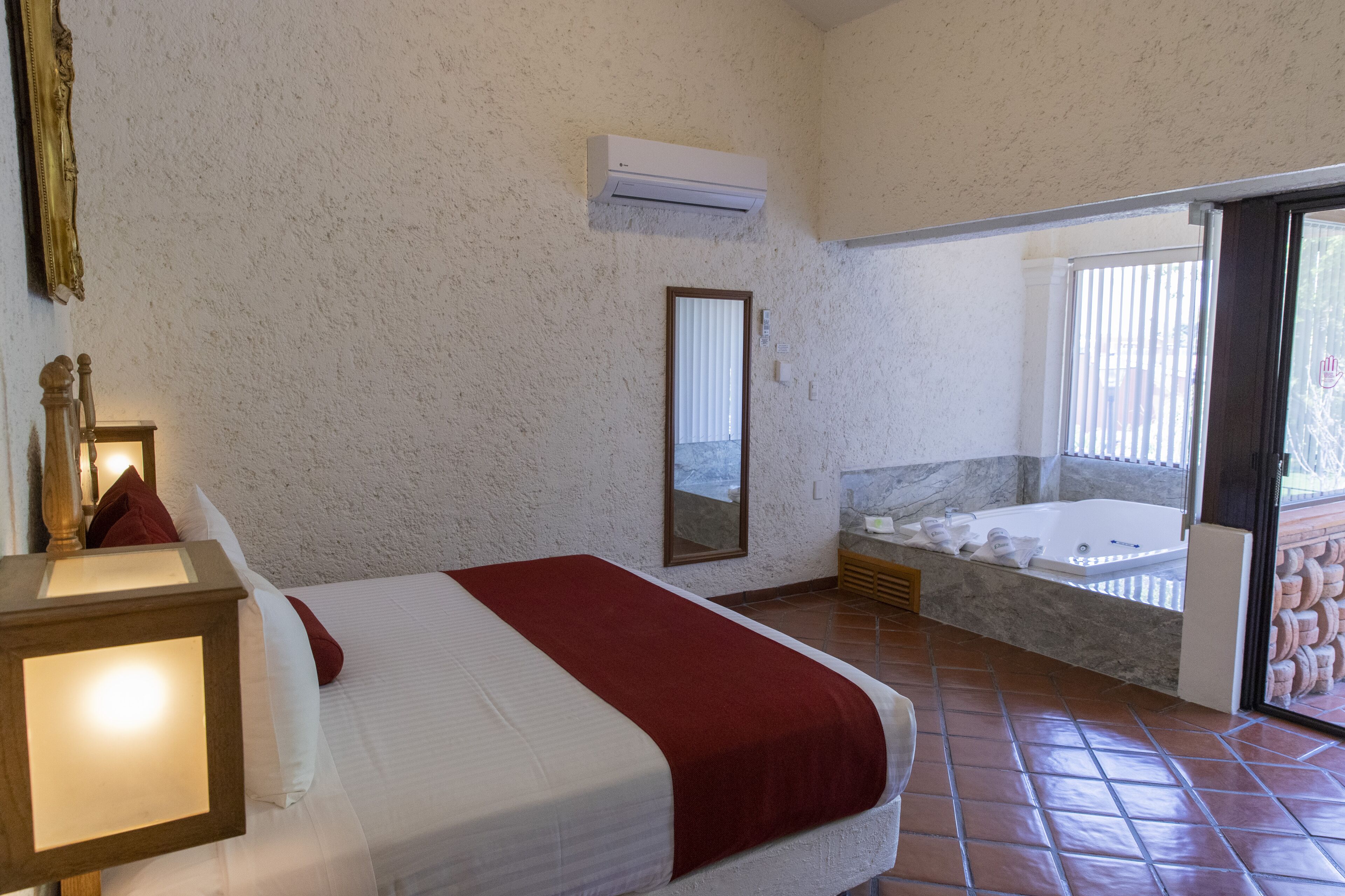 A bedroom with a bed, a large window, a bathtub, and a sliding glass door leading to an outdoor area.