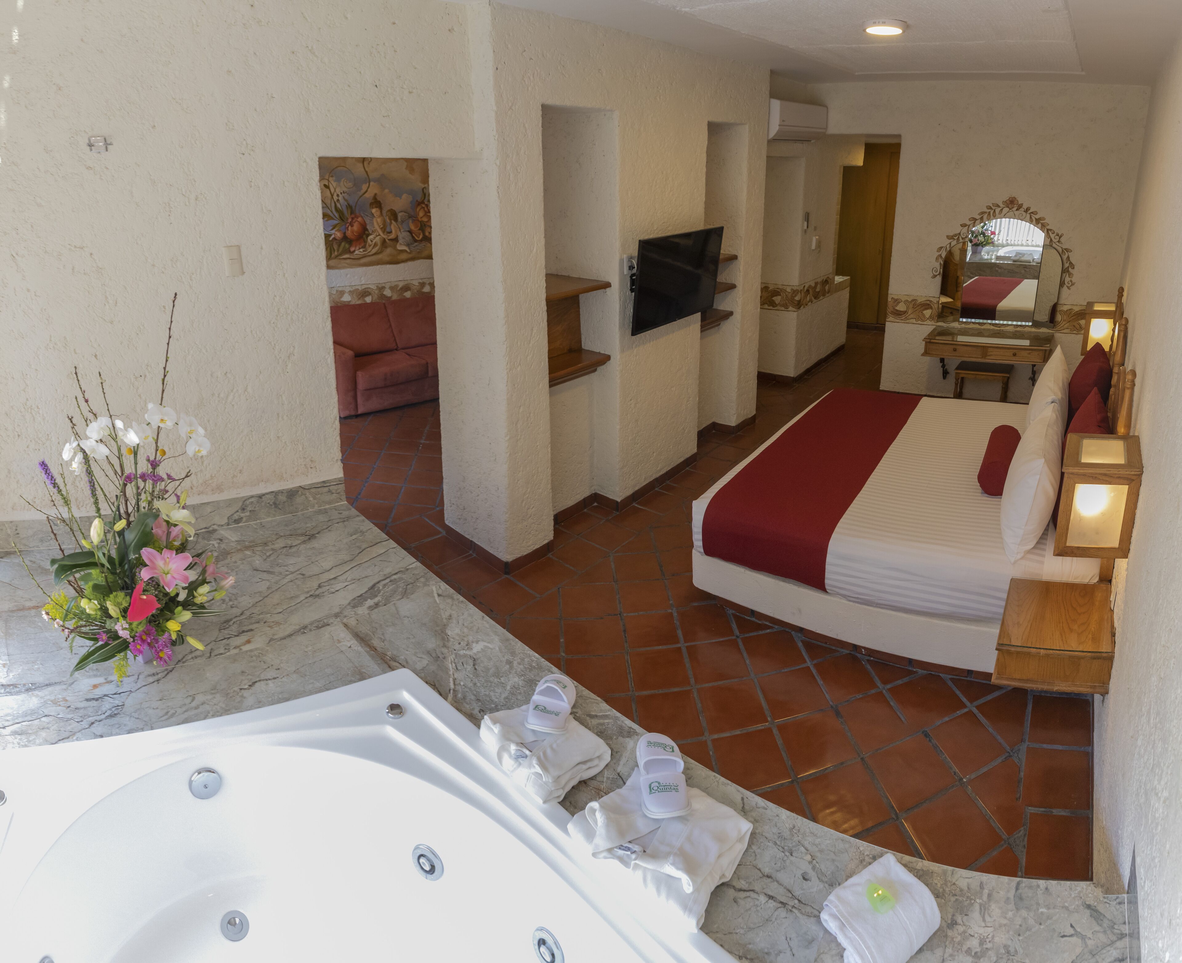 Une chambre d’hôtel avec un grand lit, une télévision, une salle de bain avec baignoire et un petit coin salon avec un canapé.
