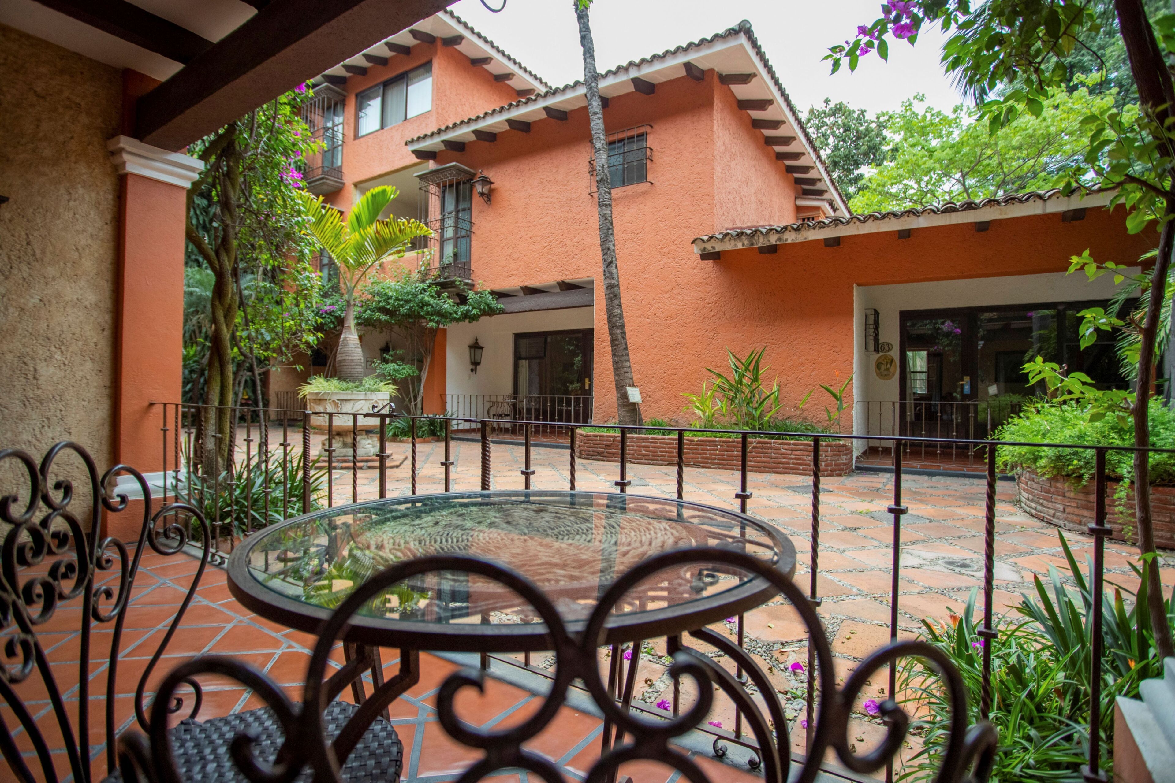 A courtyard with a glass table and chairs, surrounded by a brick wall and potted plants.