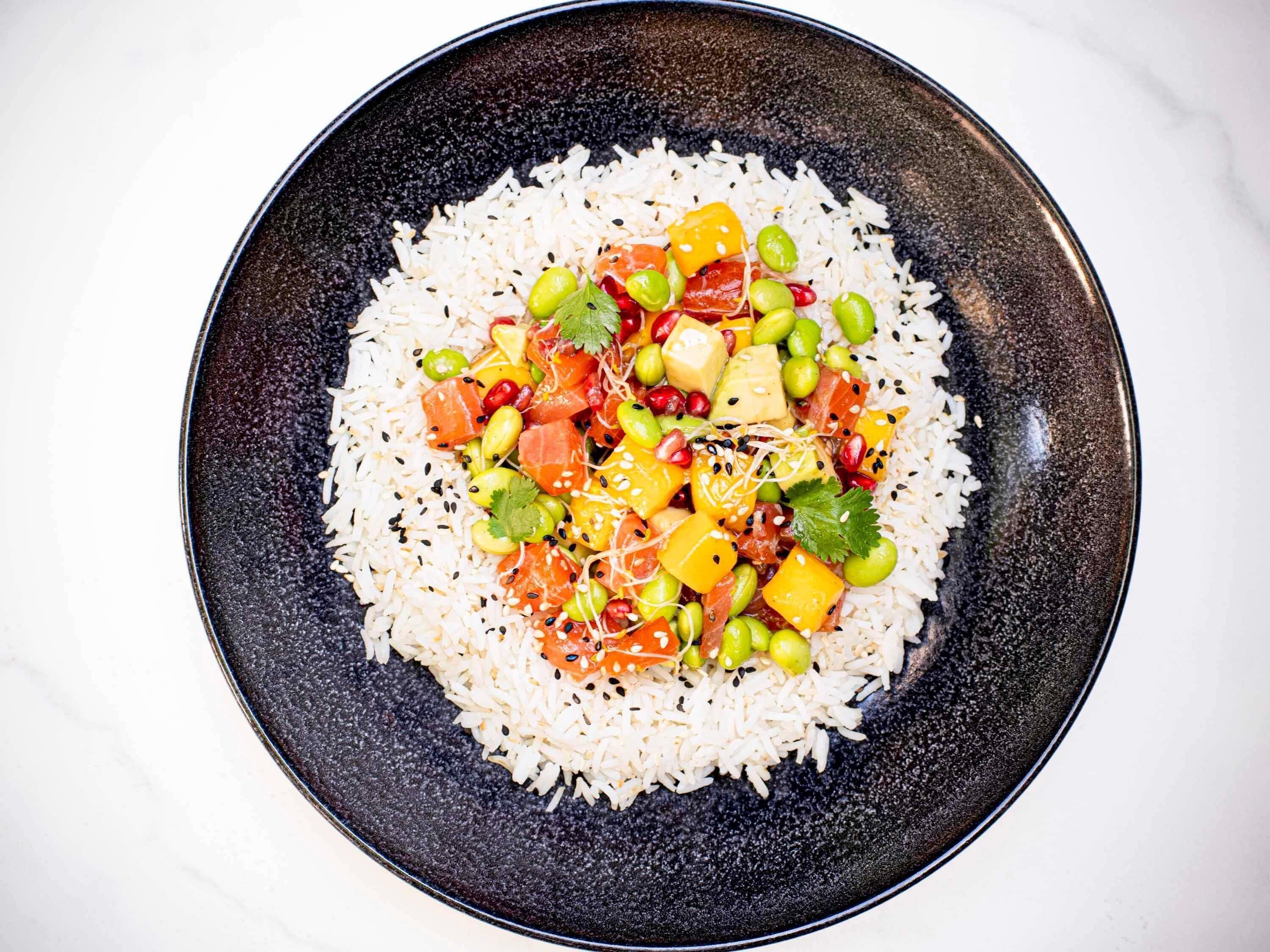 A bowl of white rice topped with colorful vegetables and fish.