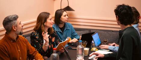 A group of people seated around a table in a conference room with laptops, a bottle of water, and a notebook.