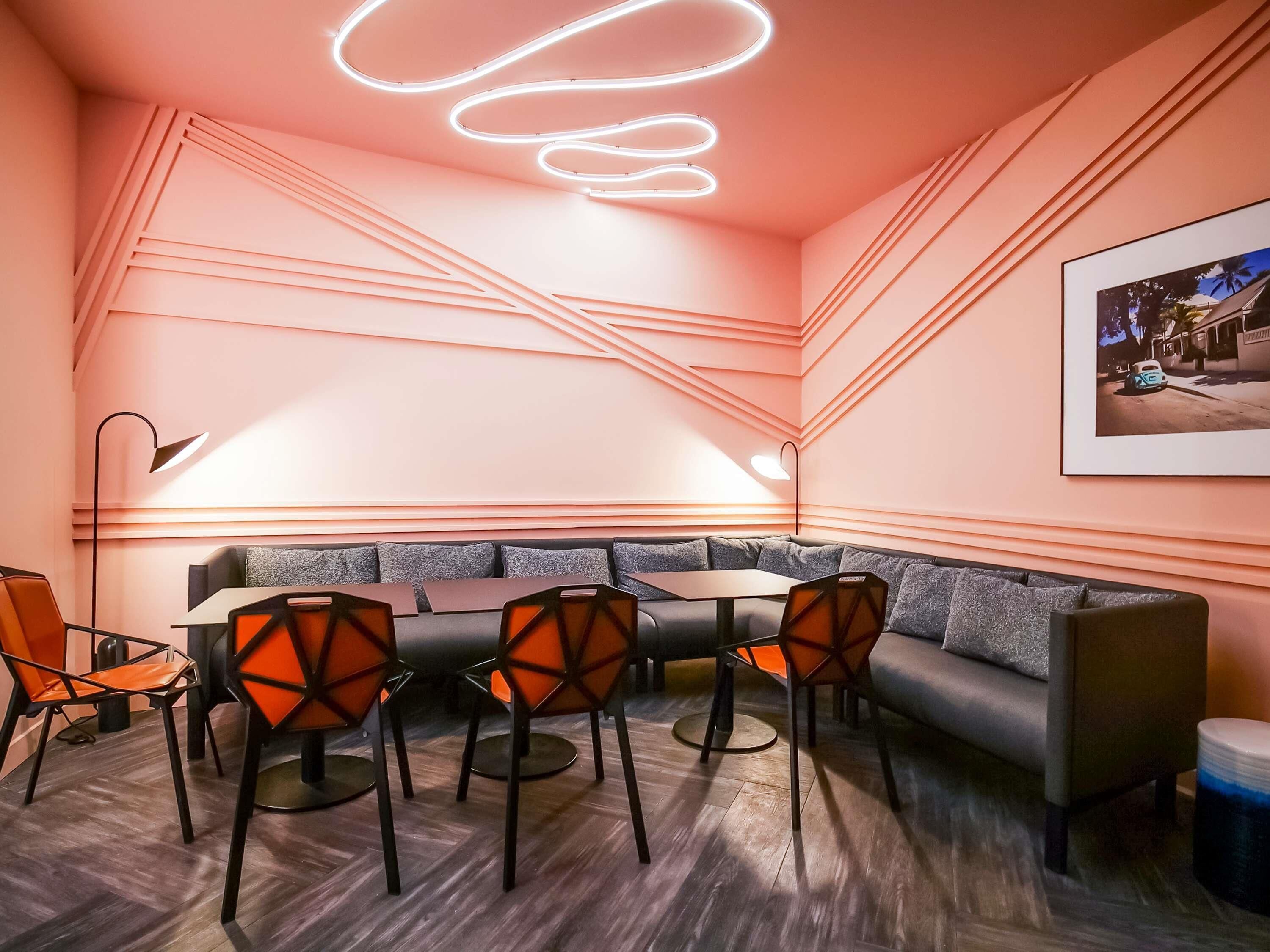 A modern meeting room with a round table, orange chairs, and a grey sofa.