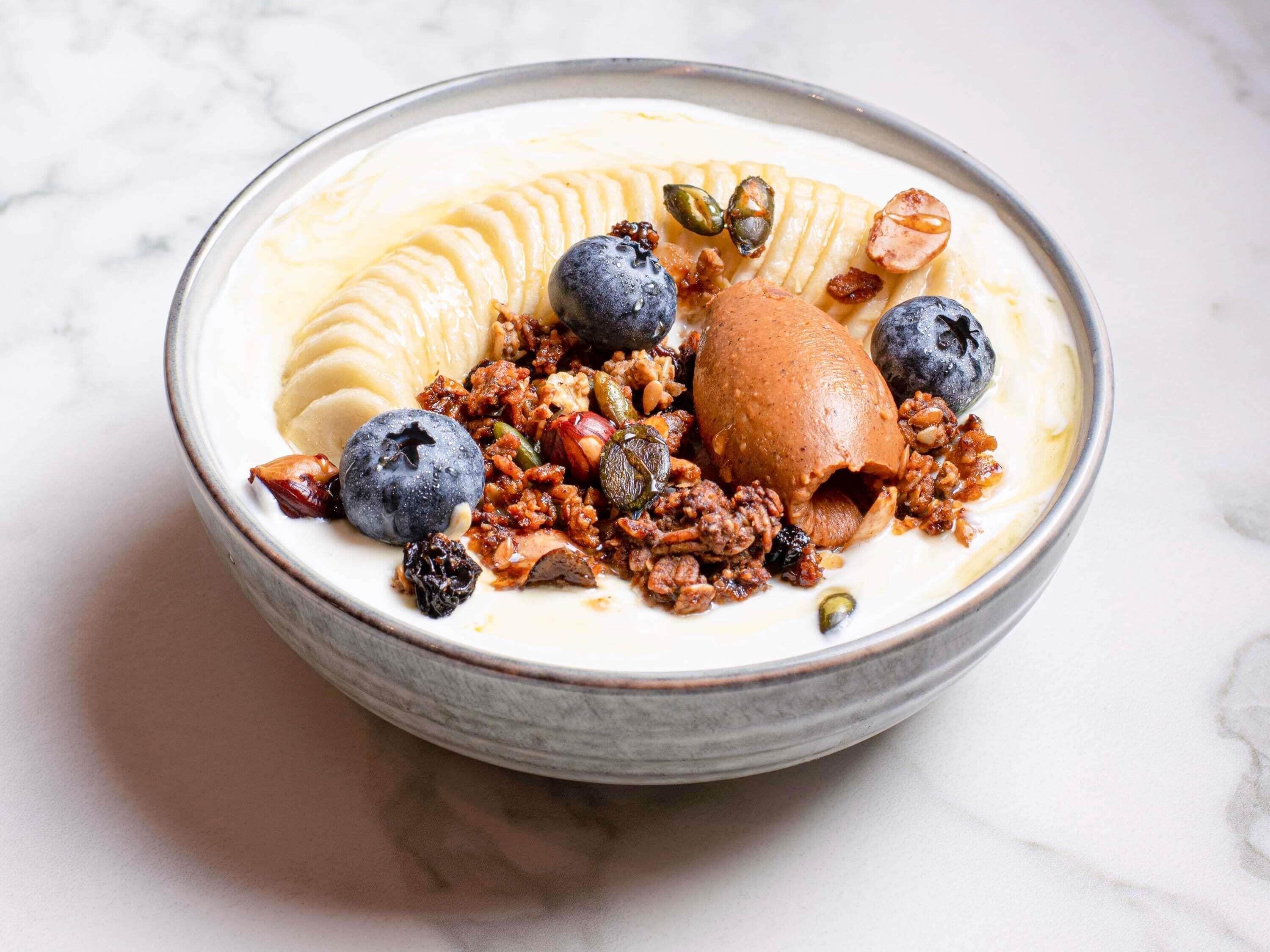 A bowl of food with a creamy base, topped with sliced bananas, blueberries, and a scoop of ice cream.