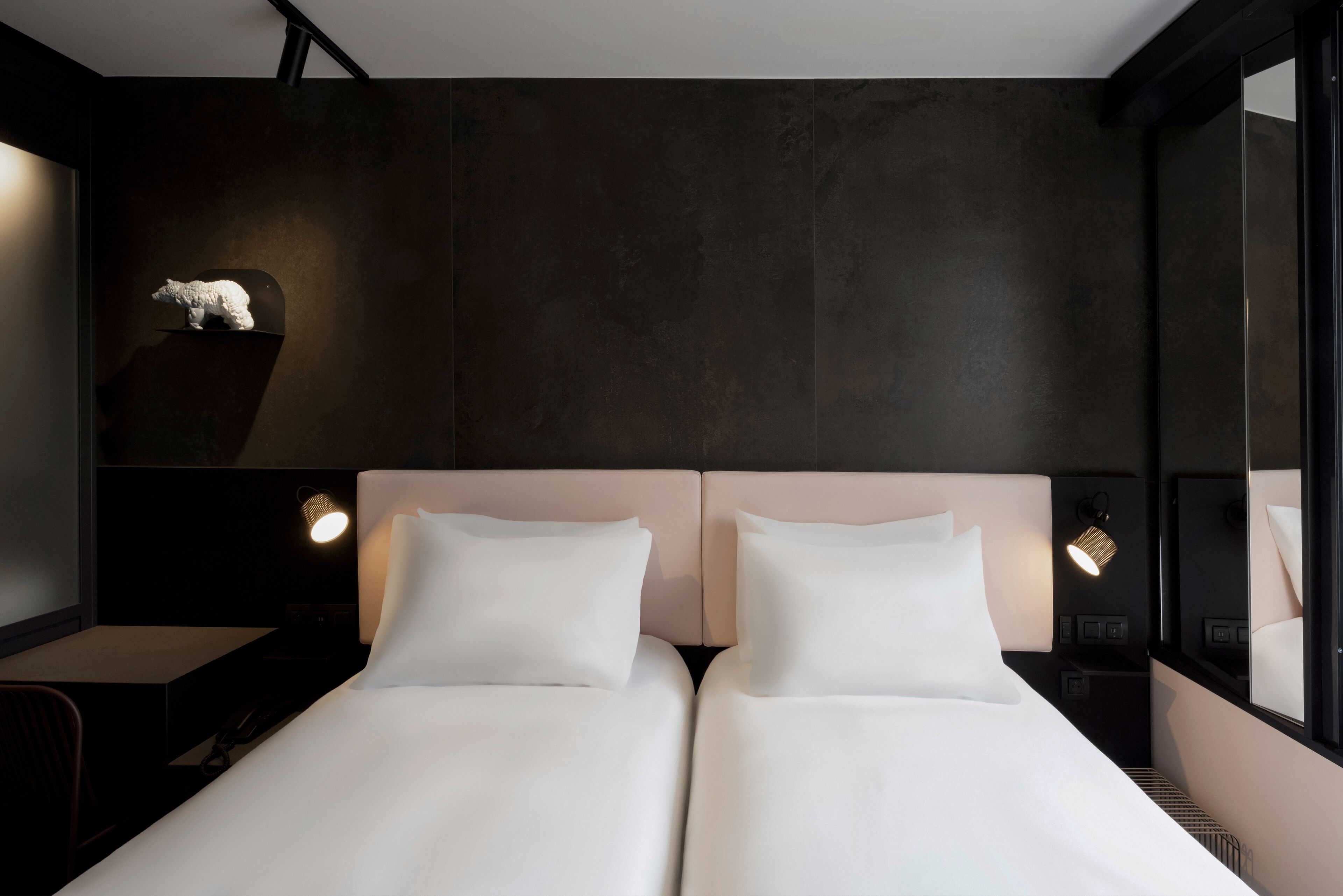 A modern hotel room with a dark wall, a white bed, and a small sculpture on the nightstand.