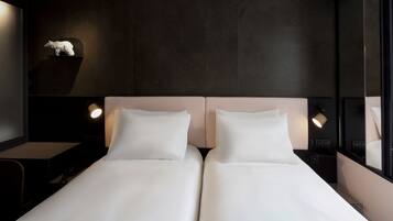 A modern hotel room with a dark wall, a white bed, and a small sculpture on the nightstand.