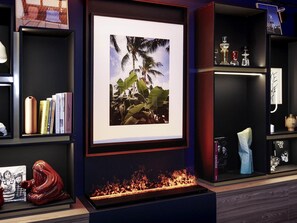 A framed picture of palm trees, a bookshelf with books, a vase, and a sculpture.