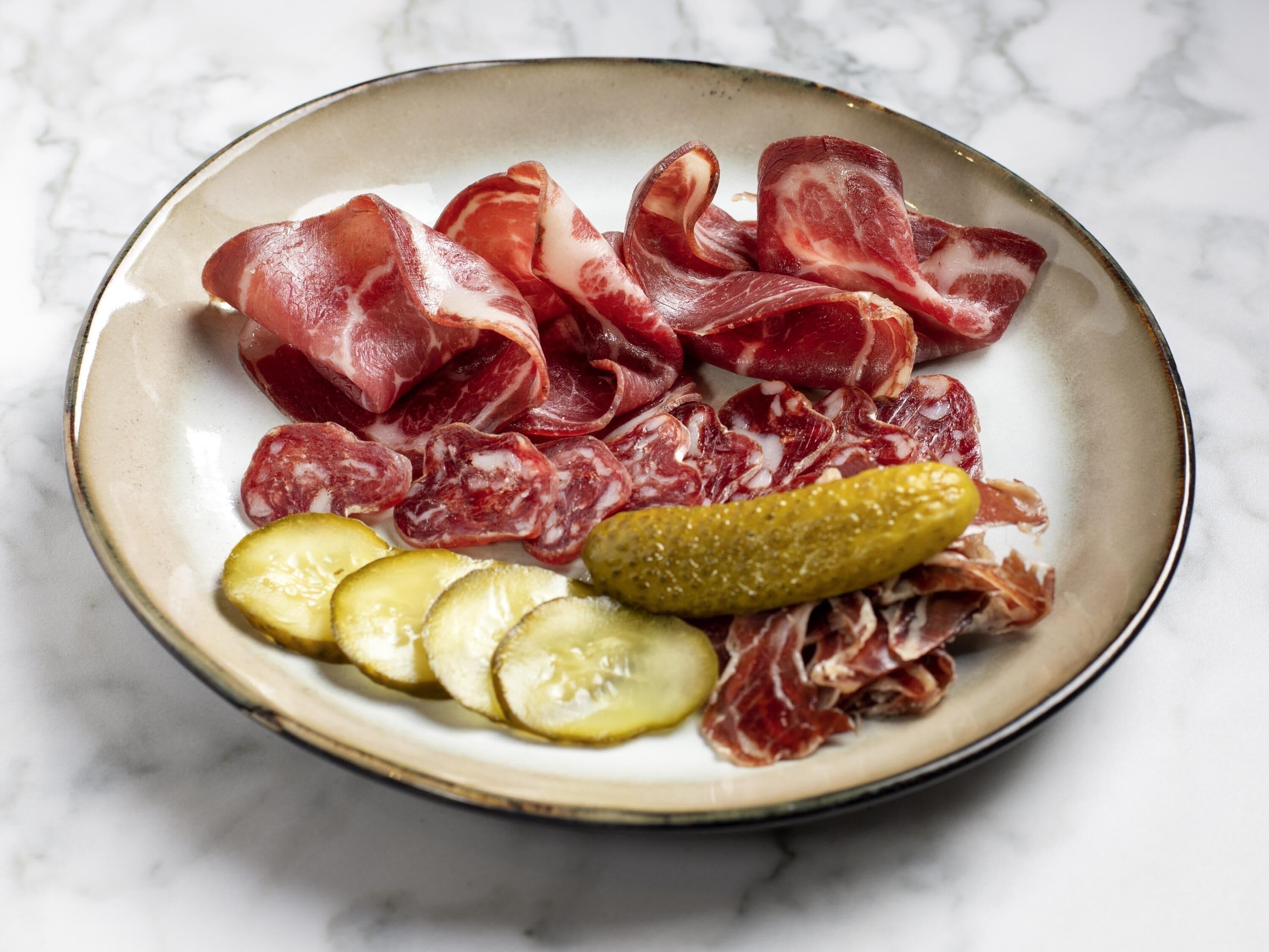 A plate with various cured meats and pickles.