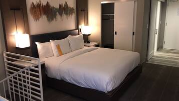 Una habitación de hotel moderna con una cama grande, dos lámparas de noche, una mesita de noche, un armario y una obra de arte colgada en la pared.