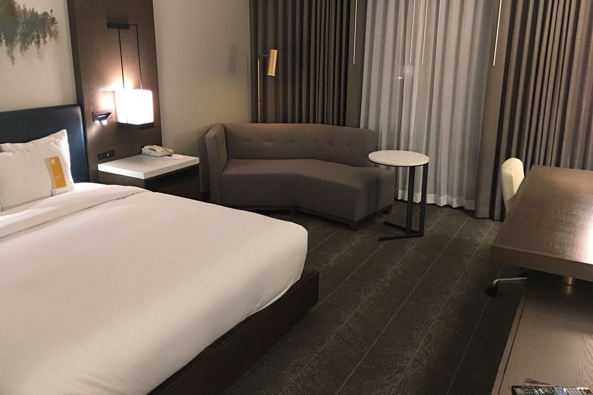 A hotel room with a large bed, a sofa, a small round table, a desk, and a chair.