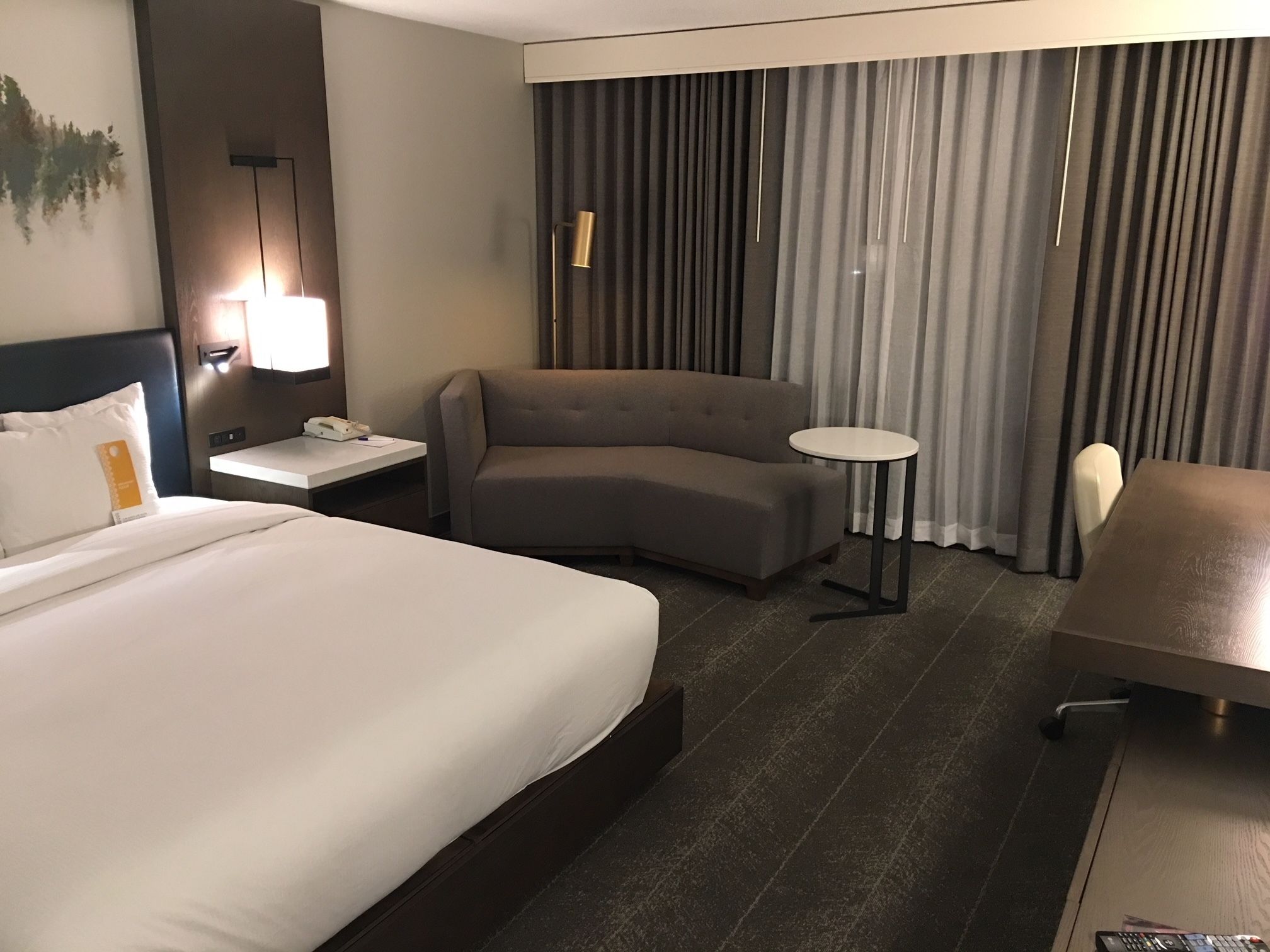 A hotel room with a large bed, a sofa, a small round table, a desk, and a chair.