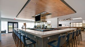 Un área de bar moderna con una isla central, taburetes y una pantalla grande.