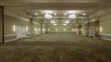 Un salón de conferencias amplio y vacío, con alfombra estampada, varias puertas y luces en el techo.