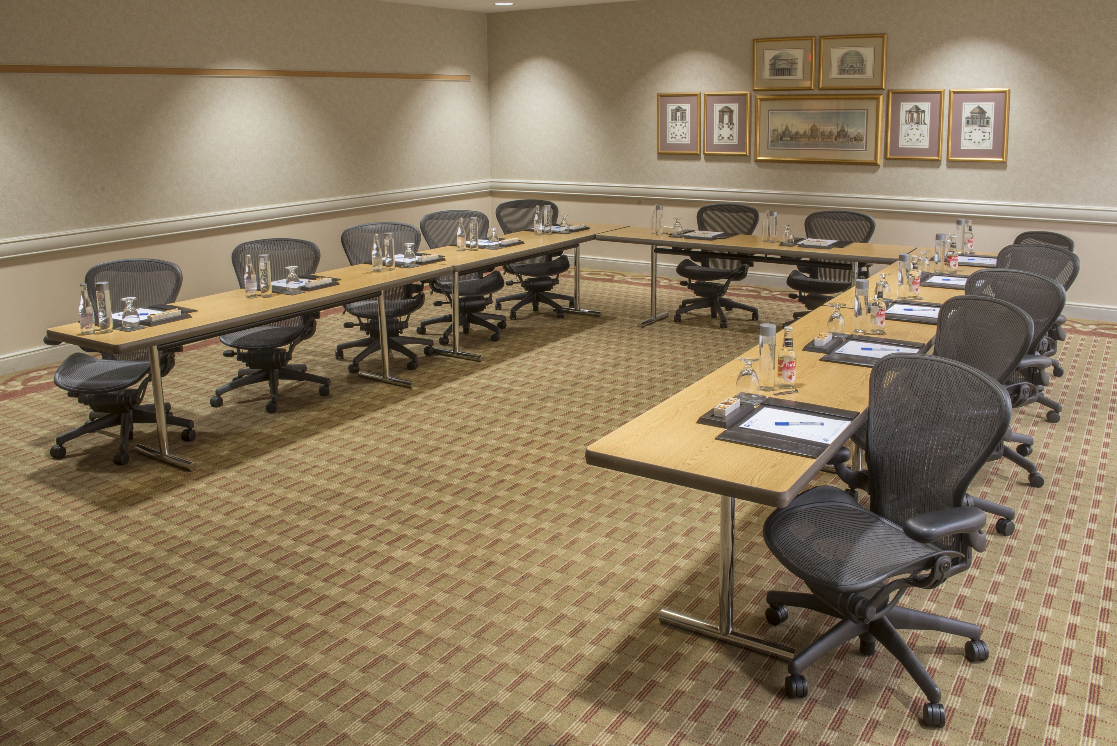 A conference room with long tables, chairs, and framed pictures on the wall.