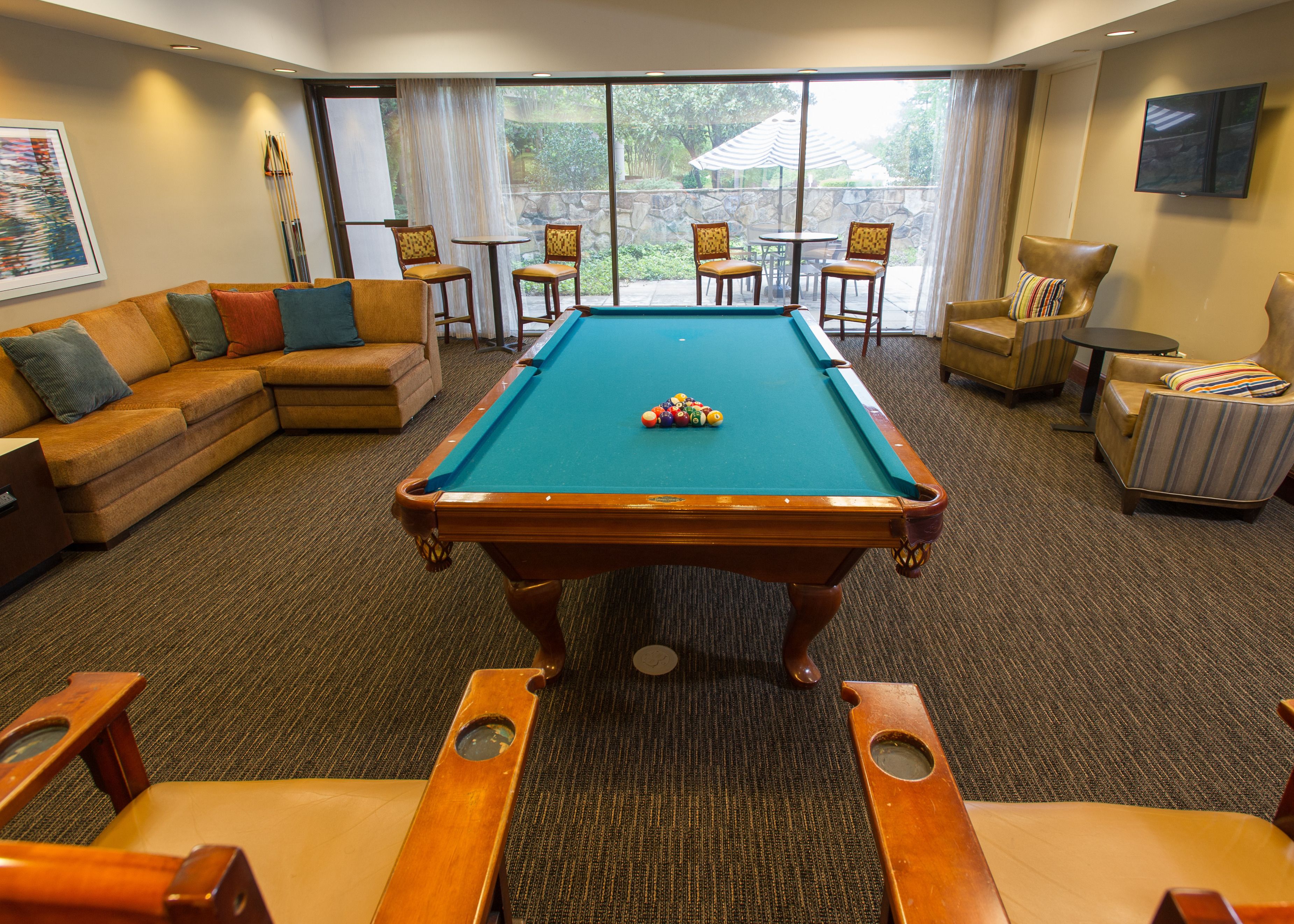 A pool table with a green felt surface, surrounded by a sofa, two armchairs, and a small table with chairs.