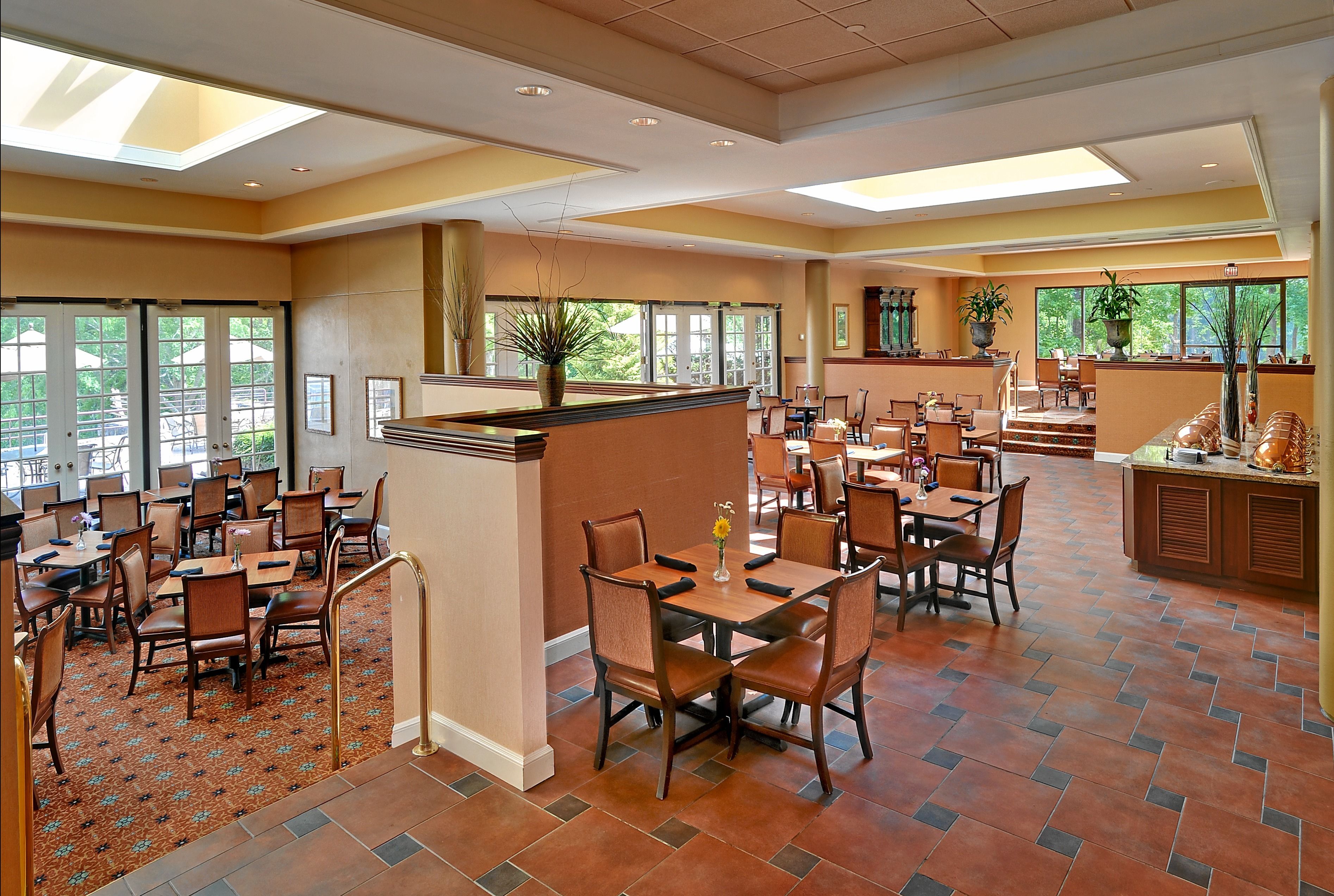A spacious dining area with multiple tables and chairs, large windows, and a central plant display.