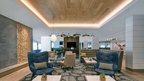 Un vestíbulo moderno con pared de piedra, zona de estar con sofás y sillones, una chimenea central y un televisor.