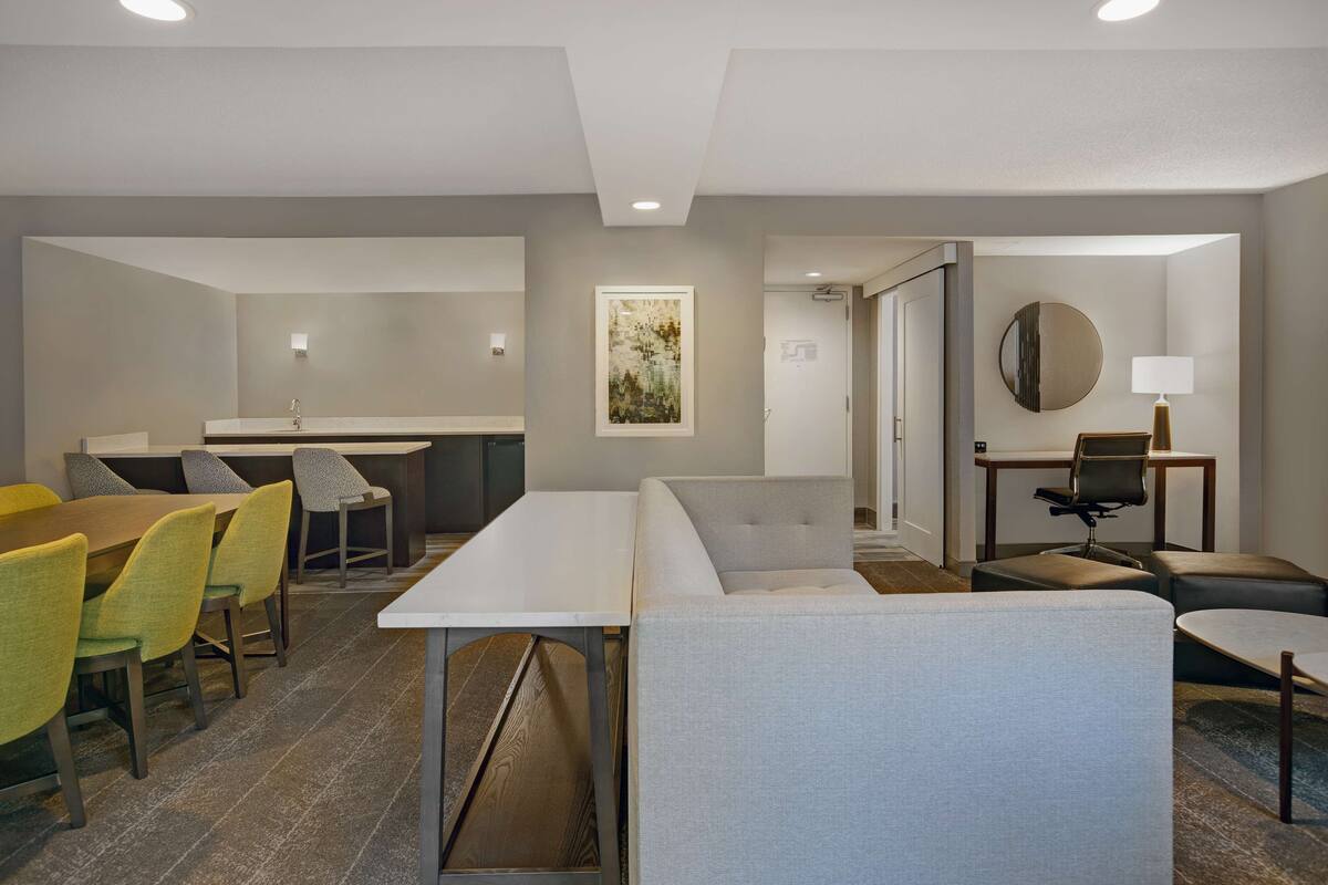 Una habitación de hotel moderna con comedor, baño privado y zona de estar con una mesa redonda y sillas.