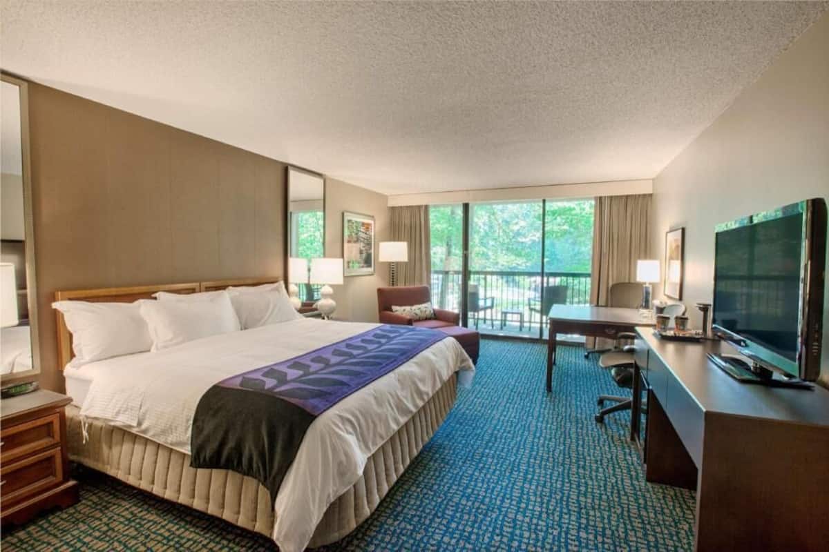 Una habitación de hotel con una cama grande, un escritorio, televisión y un balcón con vistas.
