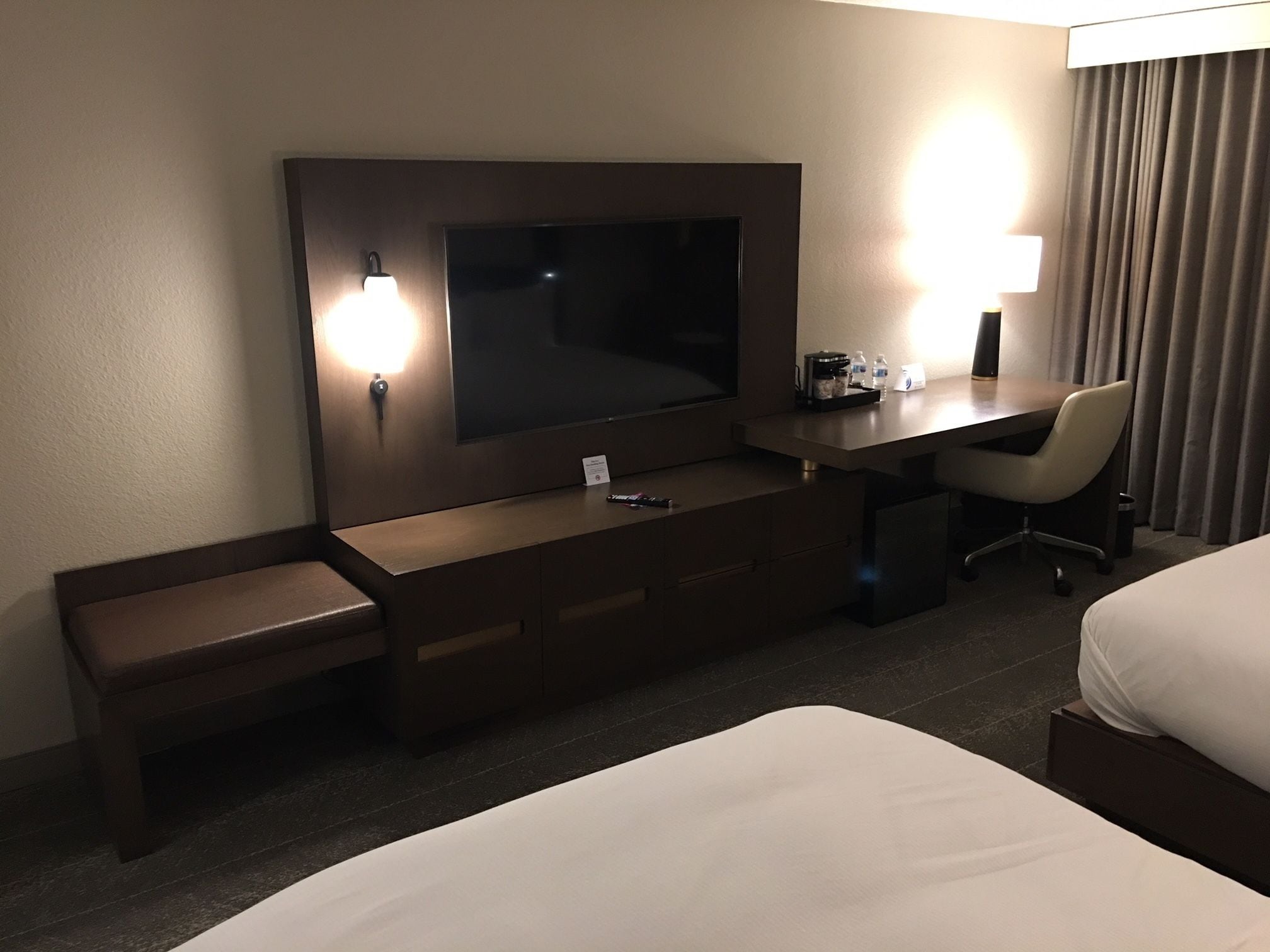 A hotel room with a bed, a desk with a chair, a TV, and a lamp.