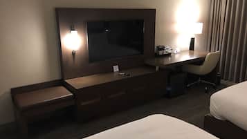 A hotel room with a bed, a desk with a chair, a TV, and a lamp.