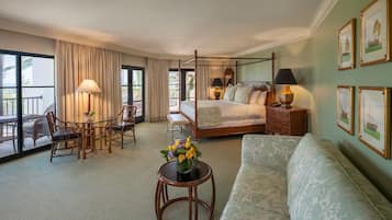 A four-poster bed, a sitting area with a sofa and chairs, a small table with a vase of flowers, and a balcony with wicker furniture.