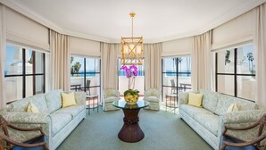 A spacious room with two sofas facing a glass table, a vase with flowers, and large windows offering a view of the ocean. - Santa Barbara Inn (Santa Barbara)