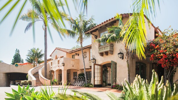 A multi-story building with a curved entrance, palm trees, and a staircase leading to the entrance. - Brisas del Mar, Inn at the Beach (Santa Barbara)