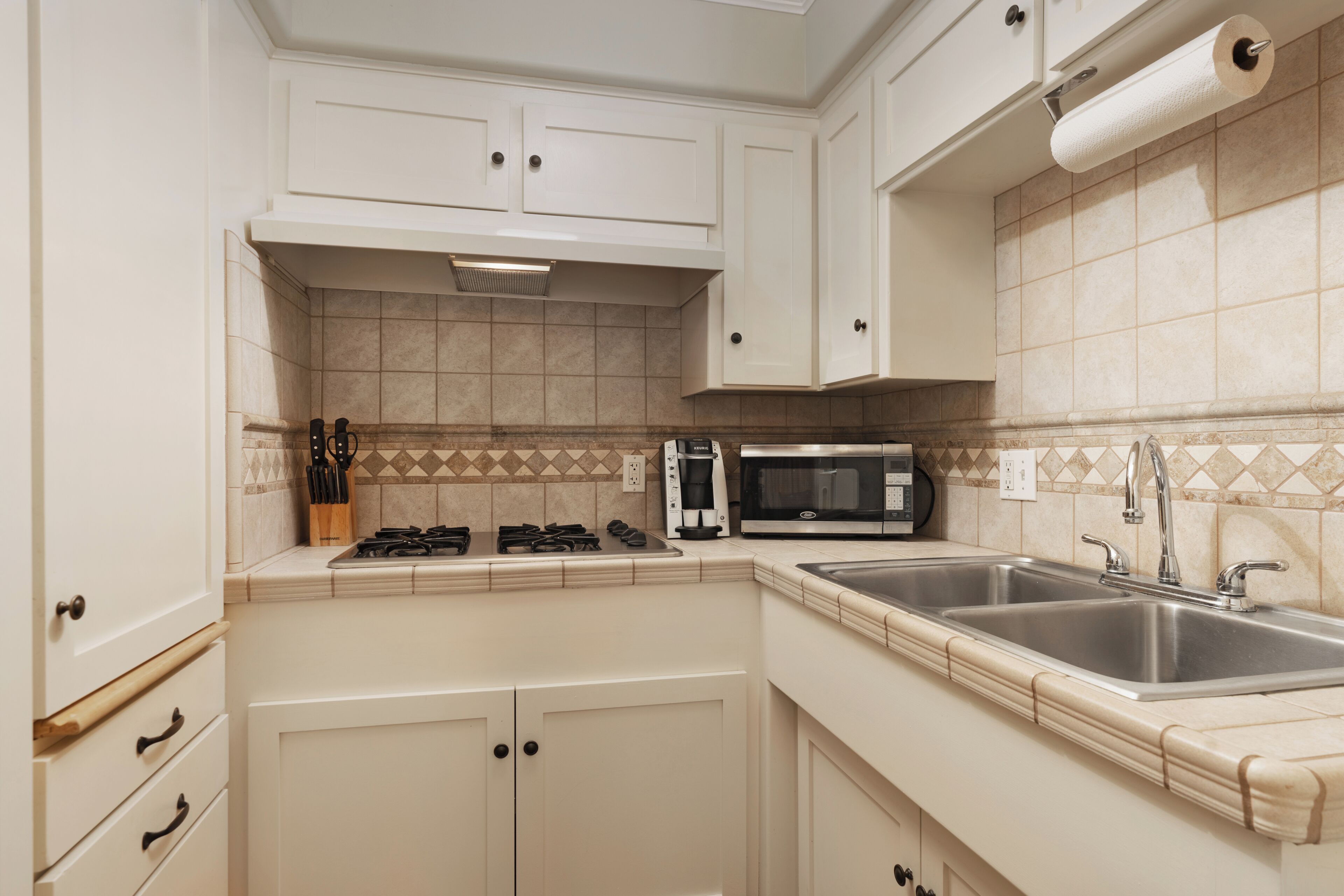 Une cuisine avec des meubles blancs, un four à micro-ondes, une cuisinière et un évier à deux bacs.