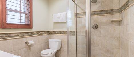 Un baño con inodoro, ducha con puertas de vidrio y ventana con persianas.