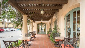 An outdoor patio with tables and chairs, a covered walkway, and a view of the street. - Brisas del Mar, Inn at the Beach (Santa Barbara)
