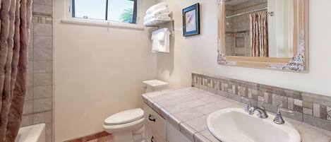 A bathroom with a bathtub, toilet, sink, and a window.
