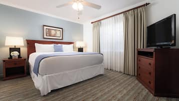 A hotel room with a bed, two bedside tables, a television, a ceiling fan, and a window with curtains.