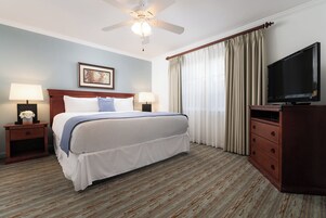Habitación de hotel con cama, dos mesitas de noche, televisión, ventilador de techo y ventana con cortinas.