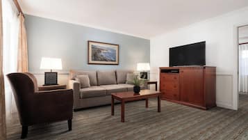 A living room with a sofa, armchair, coffee table, TV, and cabinet.