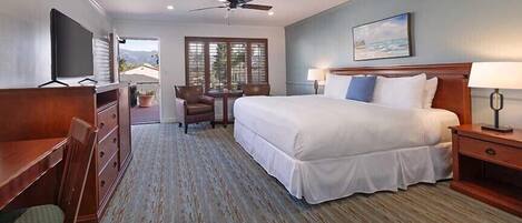 A hotel room with a bed, desk, chair, and a view of the outdoors.