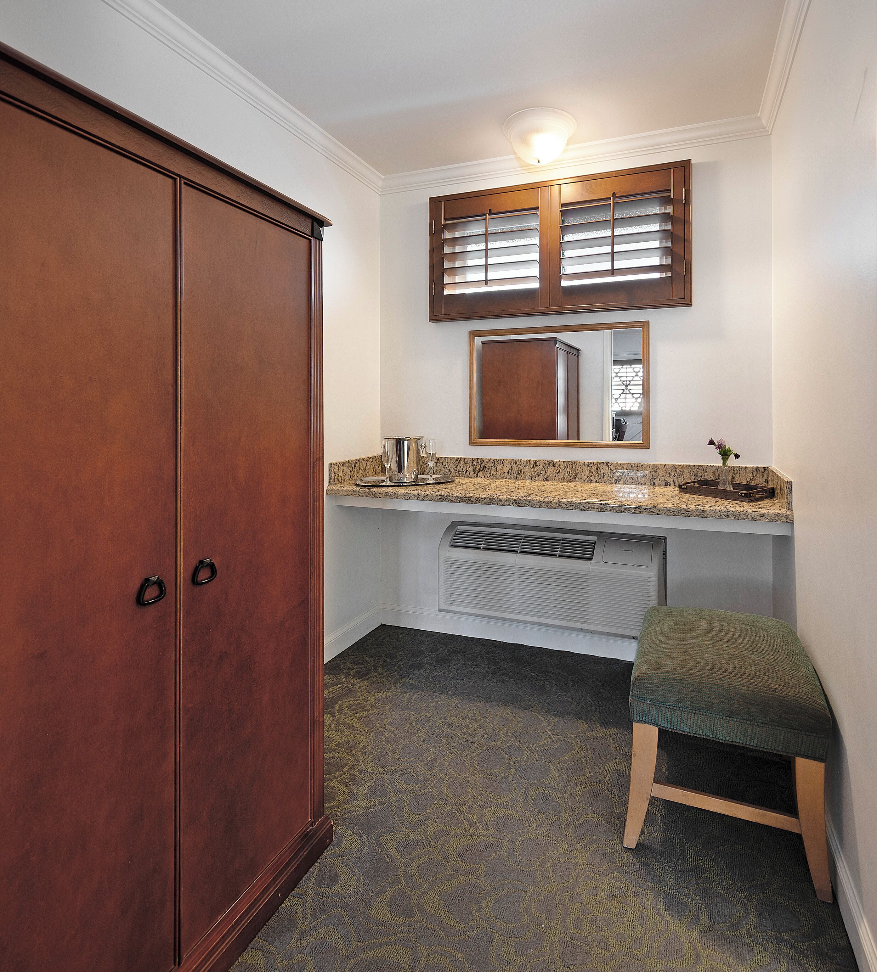 Une salle de bain avec une armoire en bois, une coiffeuse avec un miroir et un petit tabouret.