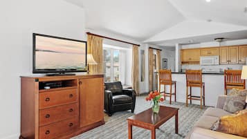 A living room with a television, a sofa, a coffee table, and a dining area with wooden chairs and a kitchen.