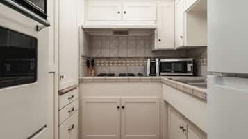 A compact kitchen with white cabinetry, a microwave, a stove, and a sink.