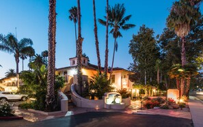 A hotel entrance with a curved driveway, palm trees, and a well-lit building facade.