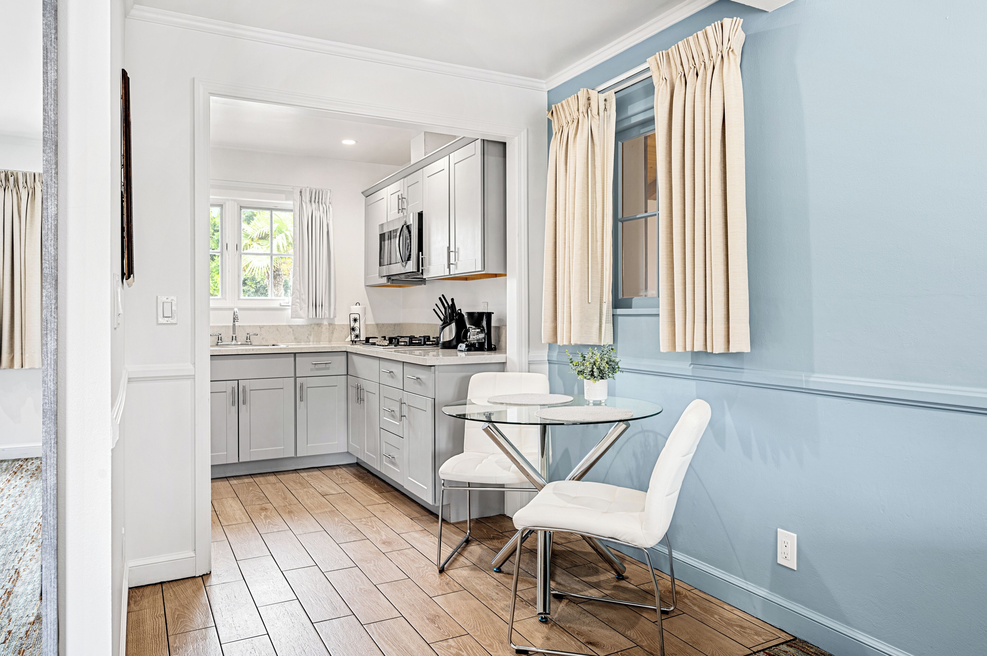 A modern kitchen with white cabinets, a microwave, and a dining area with a glass table and white chairs.