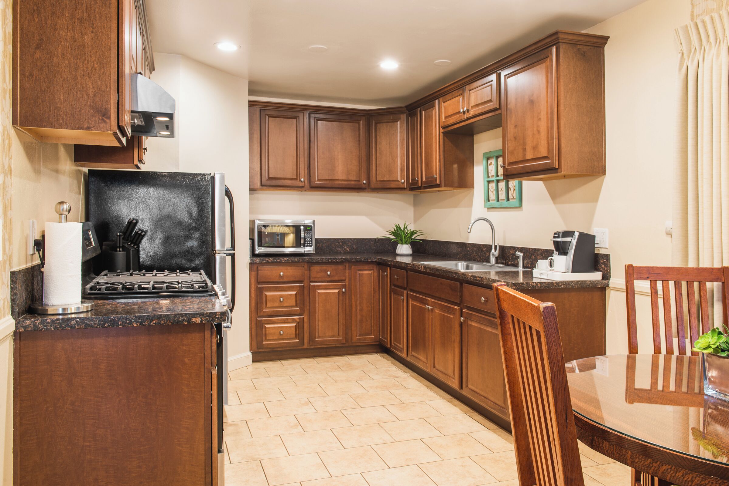A kitchen with wooden cabinets, a microwave, a stove, and a dining area with a table and chairs.