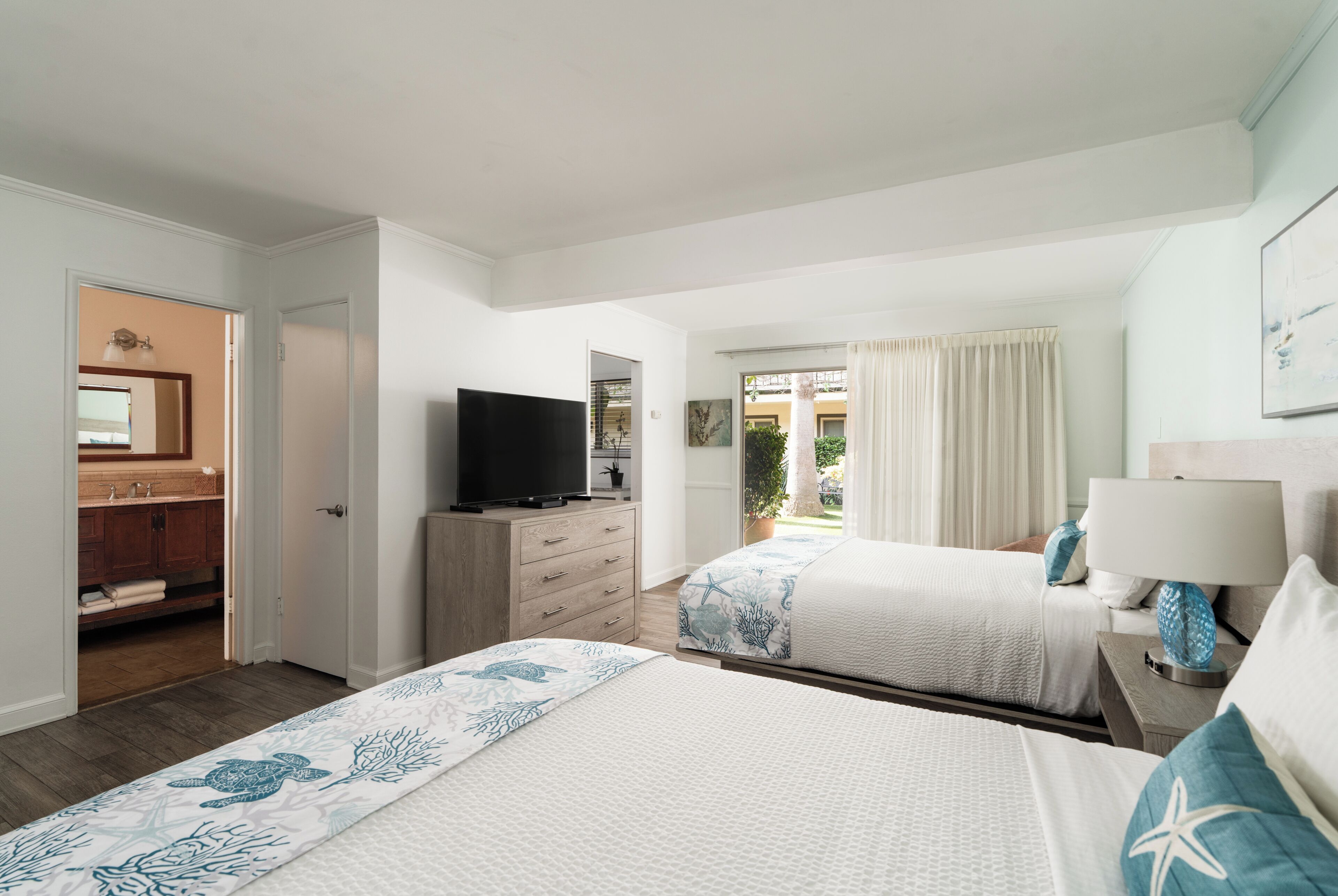 Une chambre d’hôtel avec deux lits, une télévision, une salle de bain avec un lavabo et un miroir, et une vue sur l’extérieur.