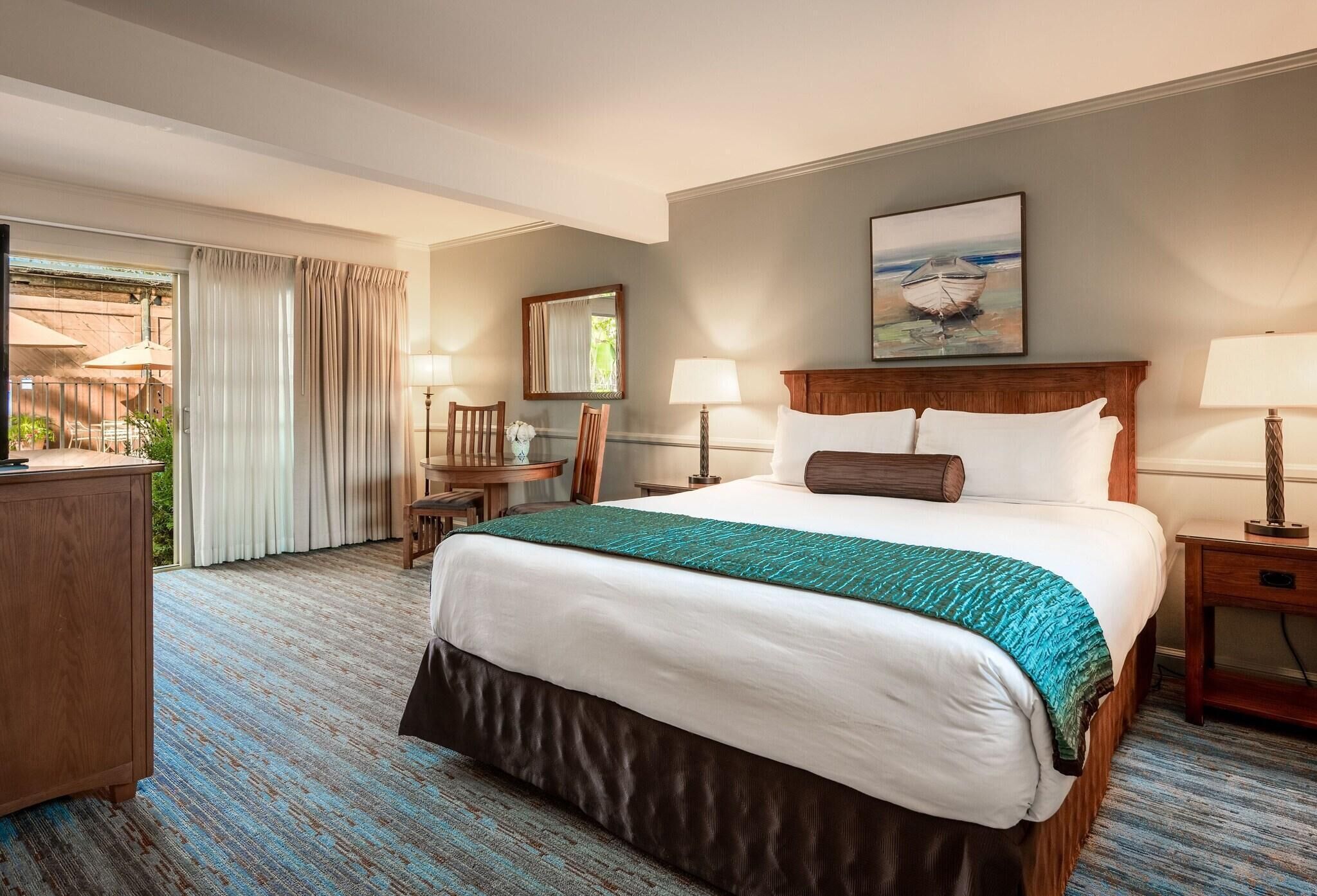 A hotel room with a large bed, a desk, a chair, and a view of the outdoors.