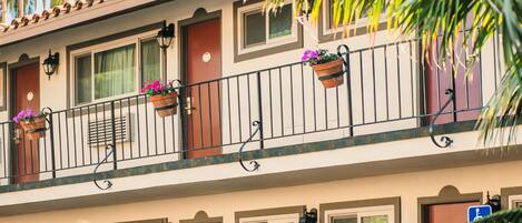 A two-story building with balconies, potted plants, and a clear view of palm trees.