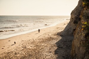 A beach with a rocky cliff and a person walking along the shore.
