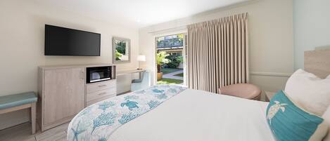 A hotel room with a bed, a desk with a flat-screen TV, a microwave, a chair, and a view of a garden through a window.