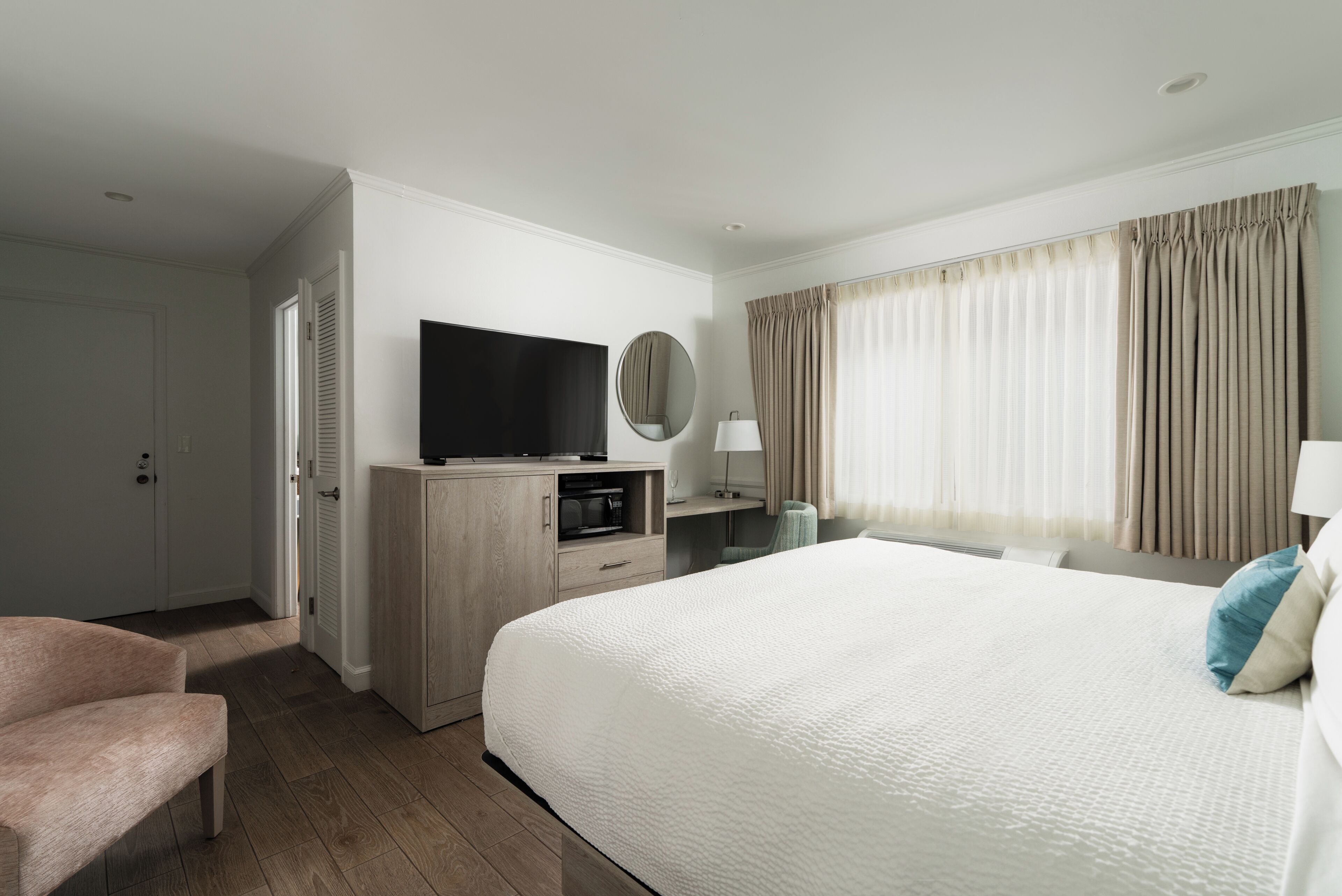 A hotel room with a bed, a TV, a desk, a chair, and a wardrobe.