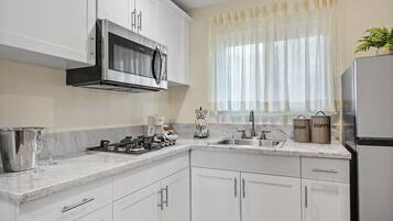 A modern kitchen with white cabinets, a stainless steel microwave, a gas stove, and a sink. There are two stainless steel containers labeled "SUGAR" and "COFFEE" on the counter.