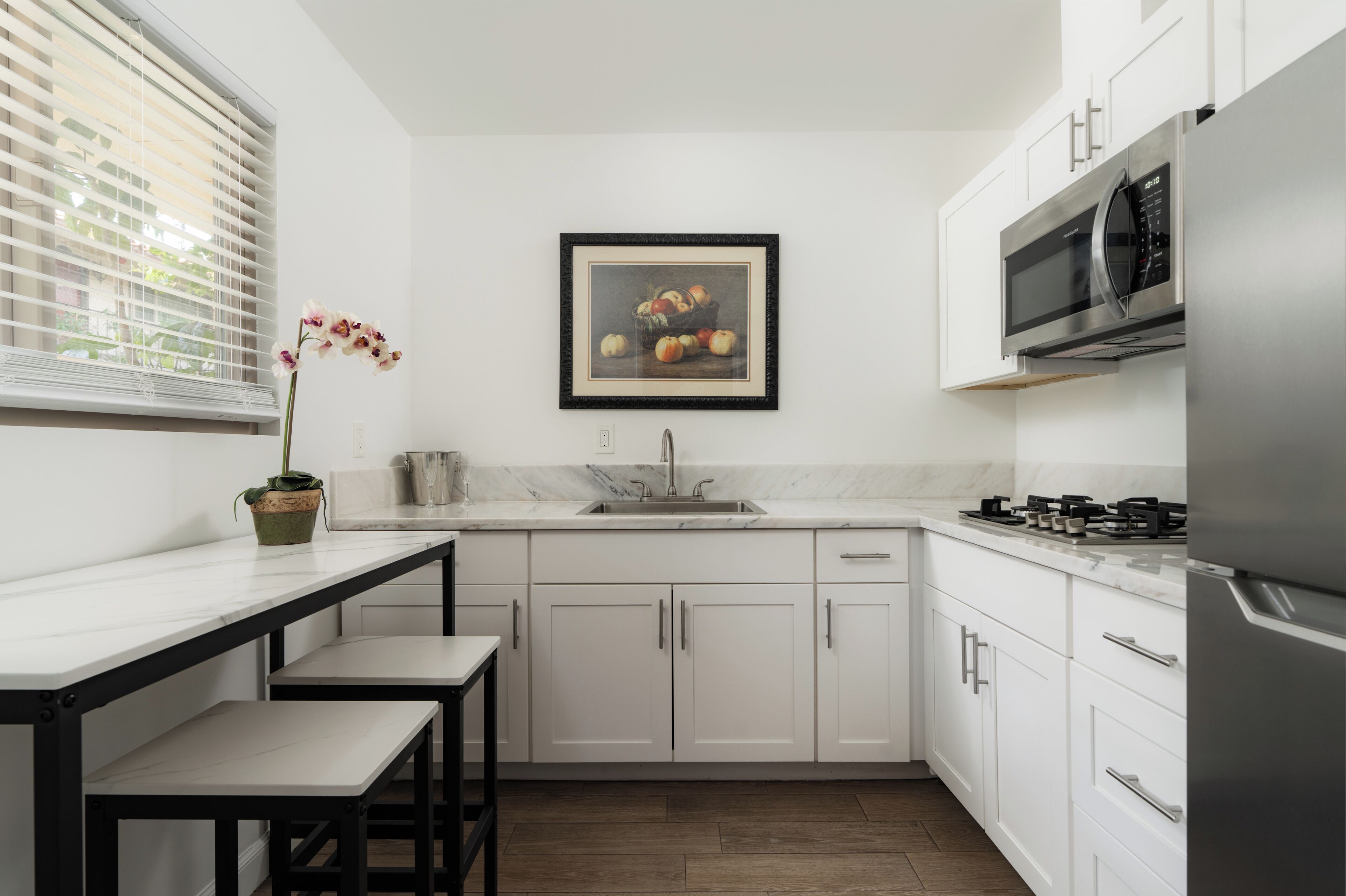 A modern kitchen with white cabinetry, a stainless steel refrigerator, a microwave, a sink, and a framed picture above the sink.