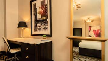 Habitación de hotel con escritorio, silla y un espejo grande. Se observa un cuadro en la pared y una pequeña planta en el escritorio.